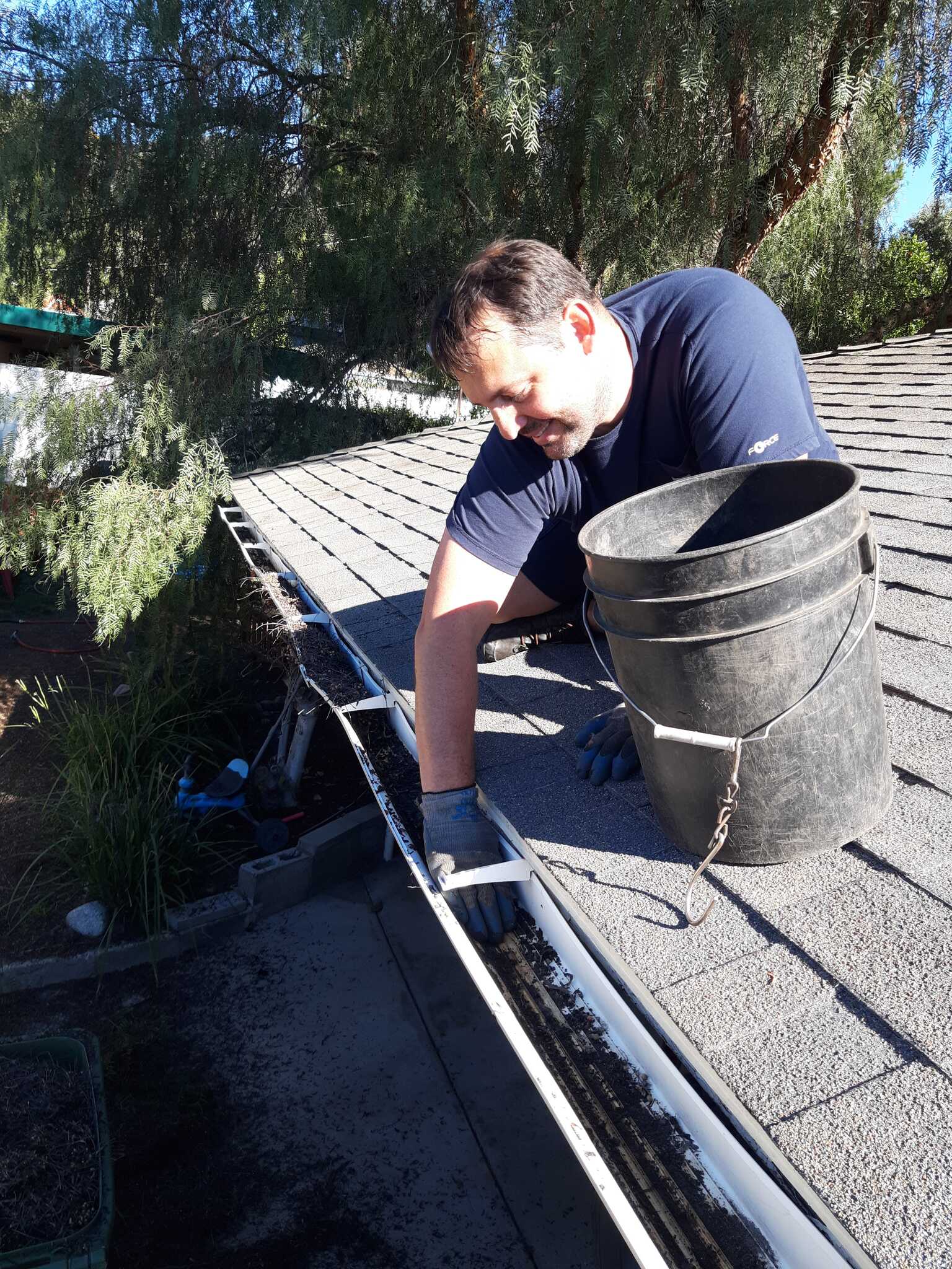 Technician cleaning a rain gutter with a bucket