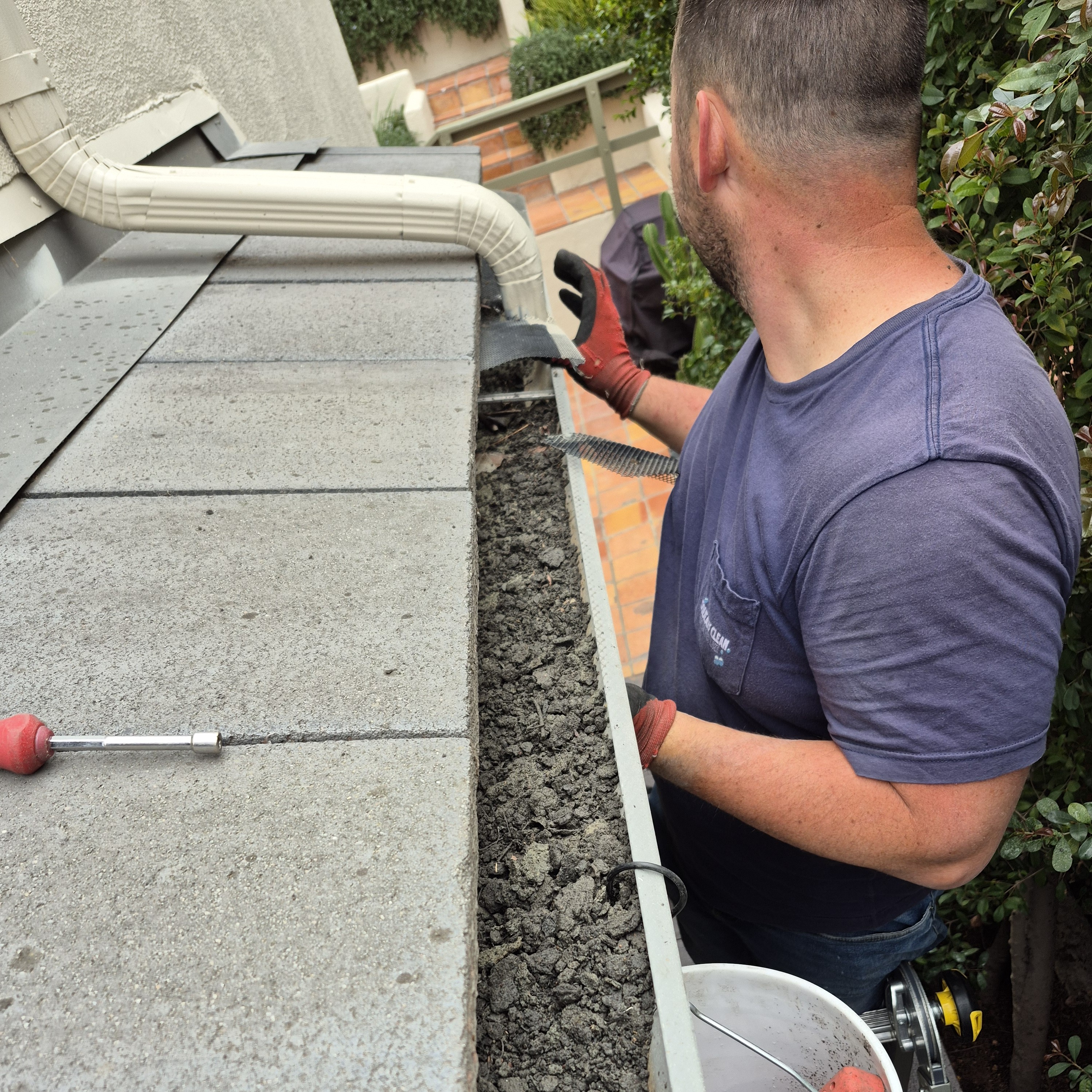 Technician using ladder cleaning a filled rain gutter